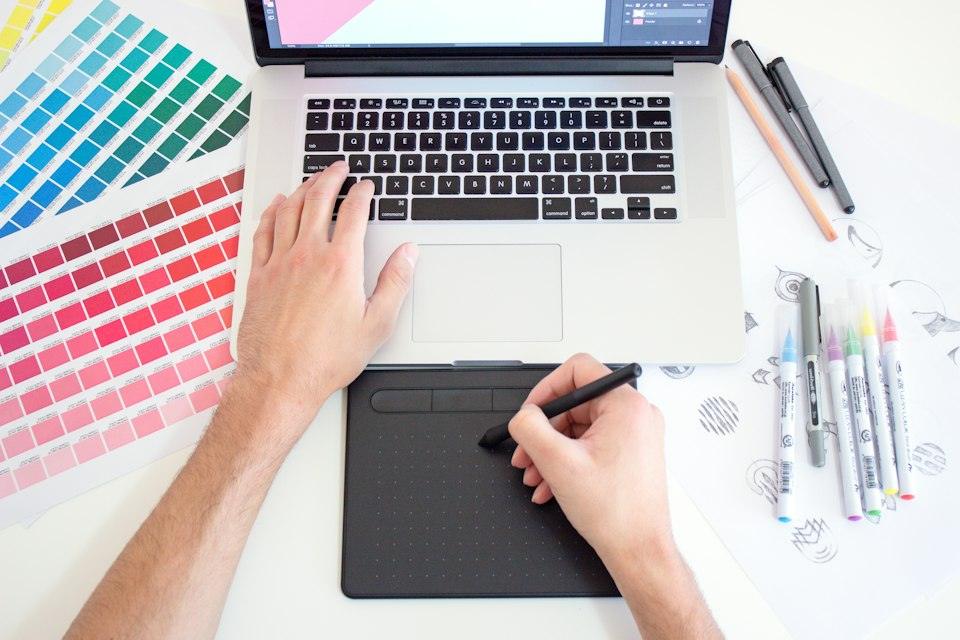 A person using a digital drawing tablet and laptop with colo